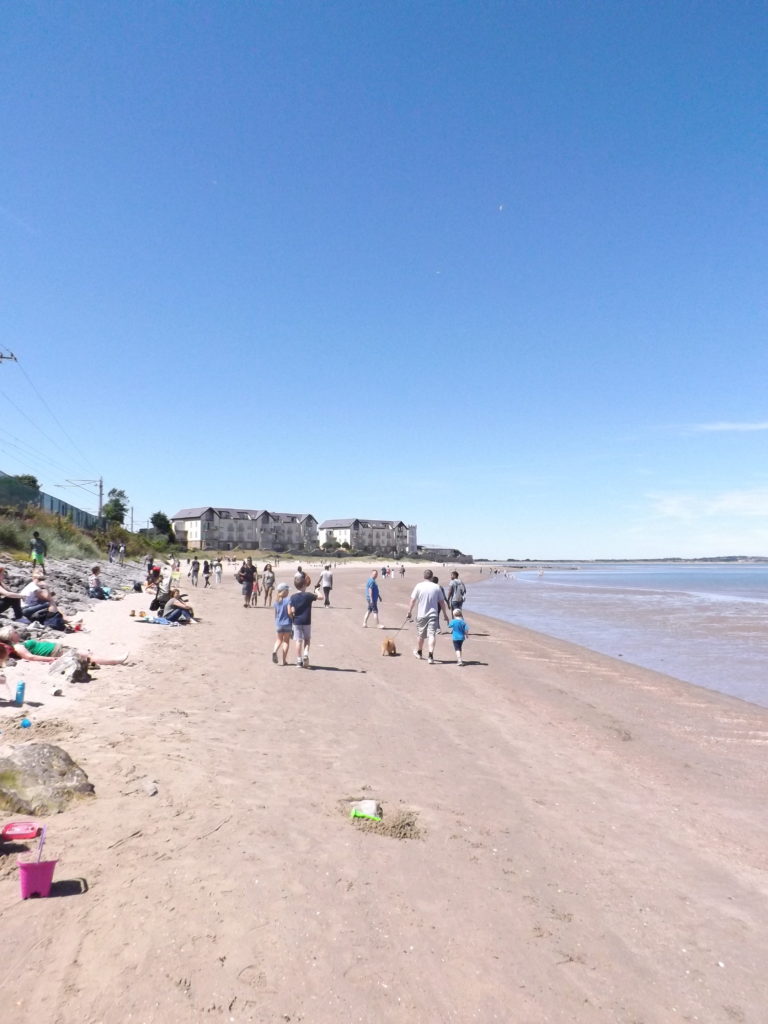 Photo de la plage de Hotwh en Irlande, le ciel est bleu et dégagé et des personnes profite de la plage.